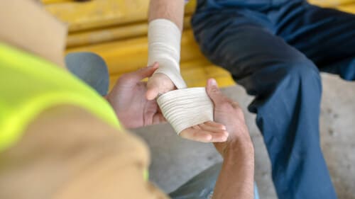 foto di un addetto al primo soccorso che medica la mano ferita di un lavoratore
