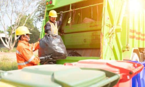 Foto di un operatore che non rispetta le norme di sicurezza del suo lavoro, salendo sul camion per gettare all'interno la busta della spazzatura