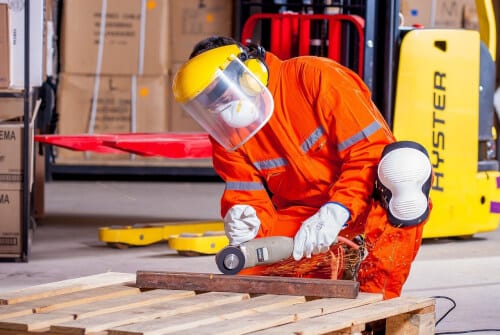 foto di un lavoratore che con tutti i dispositivi di protezione taglia un bancale in legno