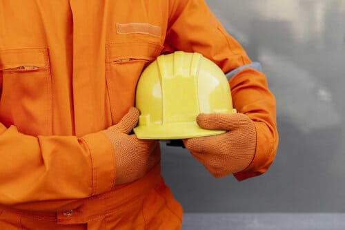 foto di un uomo vestito con tuta antincendio arancione e con casco giallo in mano
