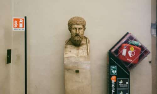 Immagine di un busto dll'antica roma con vicino la segnaletica degli estintori e una cassetta primo soccorso