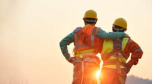 foto di due lavoratori di schiena che si abbracciano al tramonto, con tutte le attrezzature di sicurezza