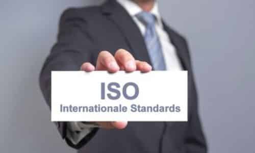 Uomo in giacca e cravata tiene in mano, davanti a se un foglio rettangolare con scritto "ISO" in grande e "Standard internazionali" in basso